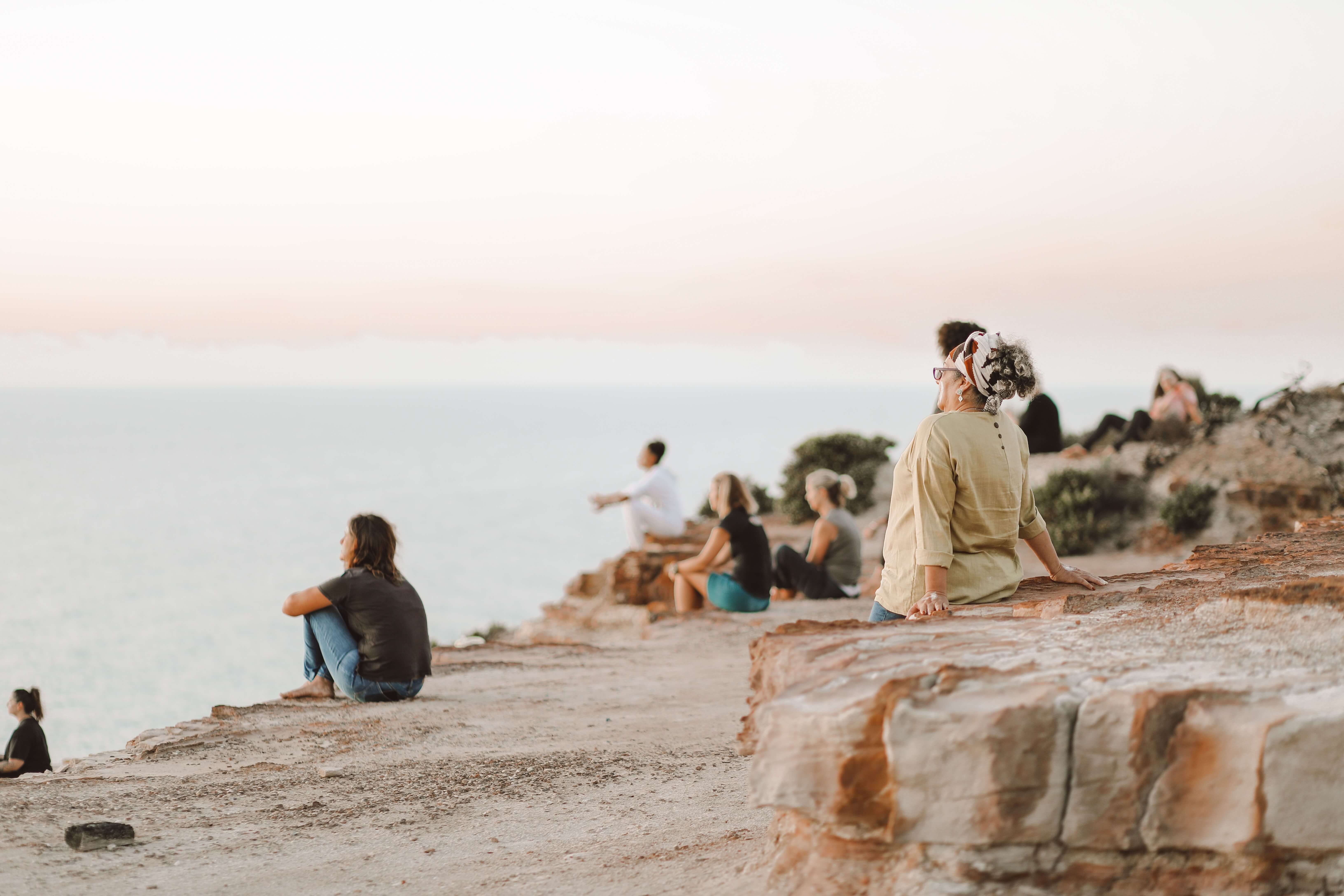A group of people sitting on a rock ledge looking out at a coastline.